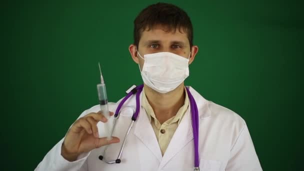 Ein Arzt hält eine Spritze in der Hand. Arzt mit Spritze auf grünem Hintergrund. — Stockvideo