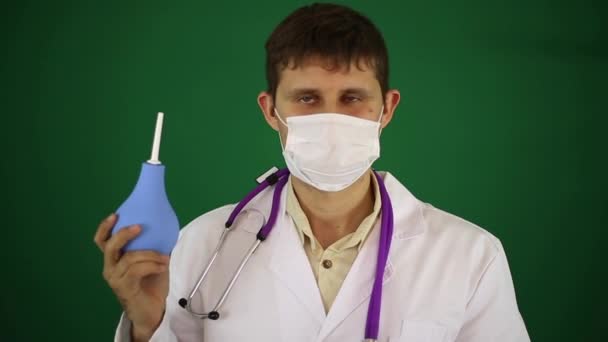 Doctor with enema on a green background. A doctor in a medical mask holds an enema. — Stock Video