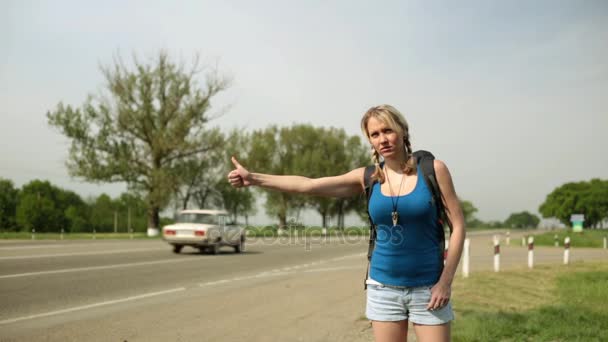 Smutná dívka zastavuje auto na silnici. Mladá žena stopování po silnici. — Stock video