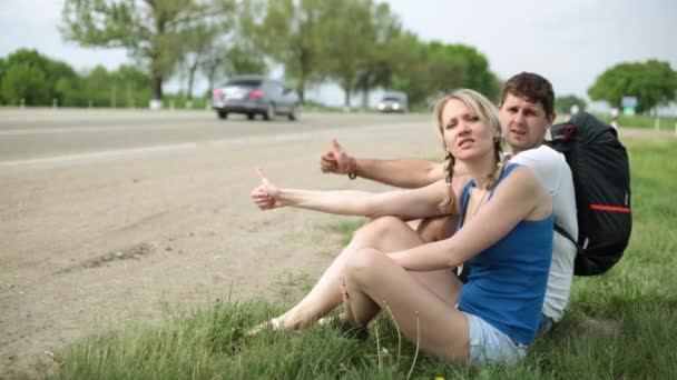 A young couple are hitchhiking. A man and a woman stop the car on the highway. — Stock Video