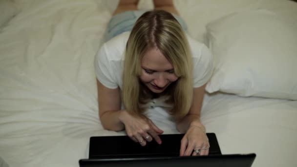 Menina com laptop na cama. Uma mulher está digitando em um laptop . — Vídeo de Stock