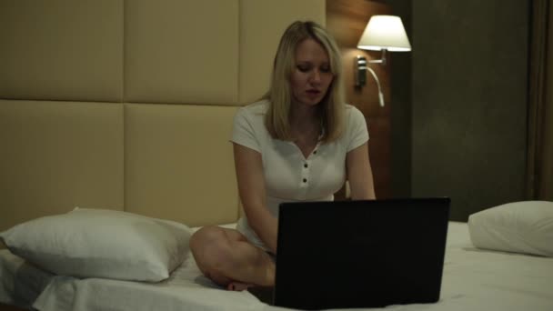 A woman is sitting with a laptop on the bed. Girl at home typing on laptop. — Stock Video