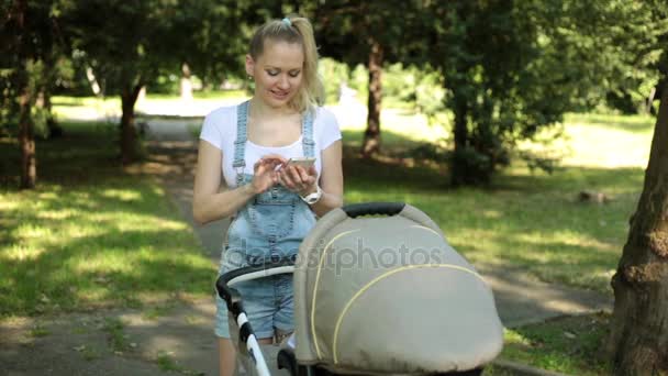 A woman with a child uses a smartphone. Mom with a baby stroller and a phone. — Stock Video