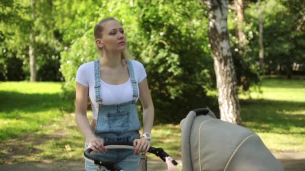 Una donna con un passeggino guarda il suo orologio. Una donna sta aspettando qualcuno. Mamma con bambino nel parco . — Video Stock