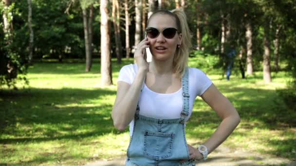 A woman is talking on the phone in the park. Beautiful girl speaks on the phone. — Stock Video
