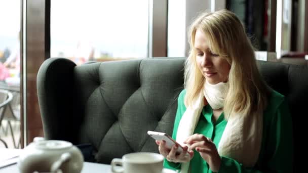 Una chica en un café con un smartphone. Una mujer marca un mensaje en el teléfono inteligente. Una chica en un café en Internet con un smartphone . — Vídeos de Stock