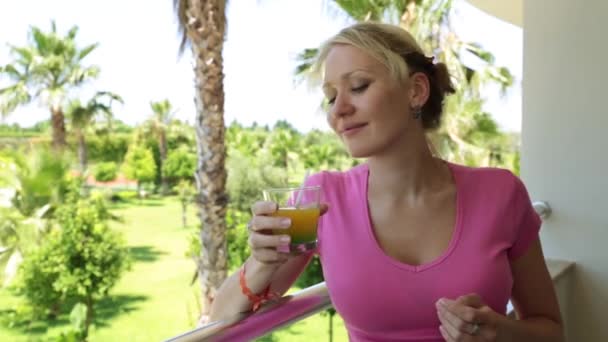 Una donna sta bevendo succo su uno sfondo di palme. Una ragazza beve un cocktail sul balcone dell'hotel . — Video Stock