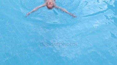 Genç bir kadın havuzda yüzüyor. Şeffaf havuzdaki kız. Sakin ol, yüzme, açık hava etkinlikleri.