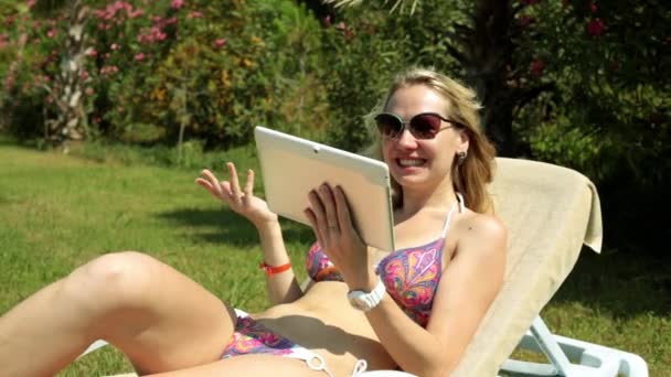 Mooie vrouw praten op skype op een strandstoel. Het meisje gaat op skype met behulp van een tablet. — Stockvideo