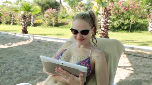 Egy lány a strandon használ egy tabletta. Szép nő, egy tabletta számítógép, a strandon. — Stock videók