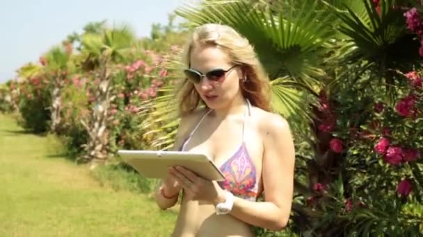 Krásná žena s tabletem v plavkách na pozadí palem. Dívka s tabletový počítač na pláži. — Stock video