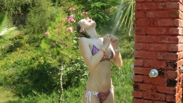 Beautiful woman in bikini takes a shower outdoors. Girl in swimsuit, tropical shower, beach and summer. — Stockvideo