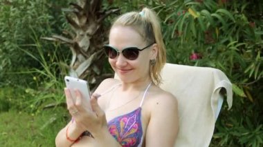 Bir bikini bir akıllı telefon ile güzel bir kadın. Sahilde kız bir akıllı telefon kullanır.