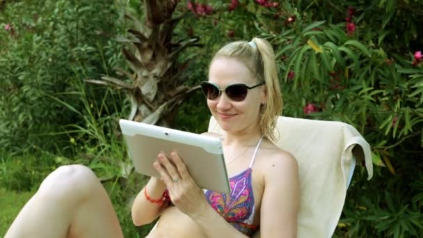 Jonge vrouw in bikini met tablet pc. Meisje in zwembroek op de achtergrond van bomen. — Stockvideo