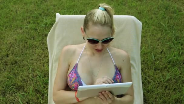 Szexi nő a bikini, a tabletta, a háttérben a zöld fű. Nő a bikini tabletta számítógép. Gyönyörű lány a fürdőruhát, egy tabletta. — Stock videók