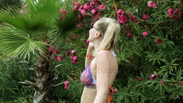 Femme sexy en bikini parlant au téléphone. Une fille parle au téléphone dans un jardin tropical . — Video