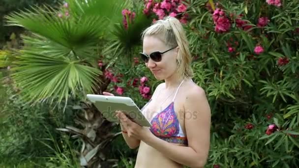 Sexy vrouw in bikini met tablet op de achtergrond van palmbomen. Meisje in zwembroek met tablet pc. — Stockvideo