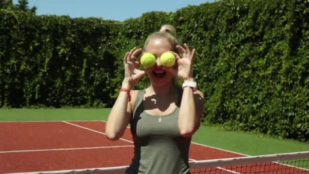 A female tennis player brings the balls to her eyes. Attractive girl on a tennis court. — Stock Video