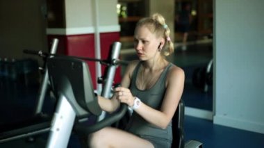 Sabit bir bisiklet sürme genç bir kadın. Bir kız bir fitness merkezinde bir egzersiz bisikleti üzerinde.