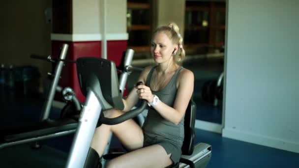 Mulher atraente está se exercitando em uma bicicleta de exercício. Menina no centro de fitness. Desportista em uma bicicleta estacionária . — Vídeo de Stock