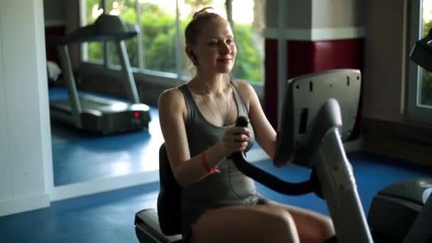 Mujer atractiva está haciendo ejercicio en una bicicleta estática. Deportiva en bicicleta estacionaria. Chica en el gimnasio . — Vídeos de Stock