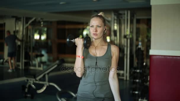 Mujer atractiva haciendo ejercicio con pesas. La rubia trina los bíceps. Chica en el gimnasio . — Vídeos de Stock