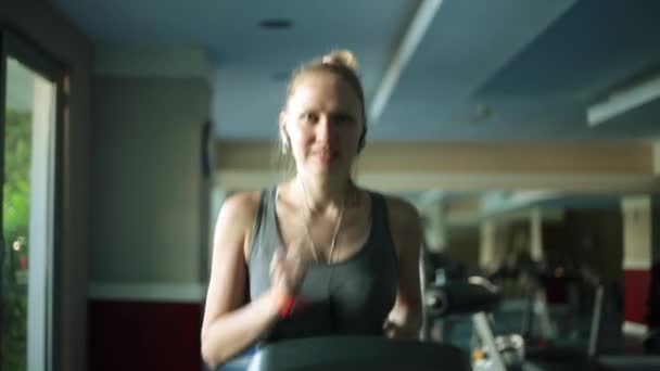 La chica está corriendo en el gimnasio. Mujer atractiva en una cinta de correr . — Vídeos de Stock