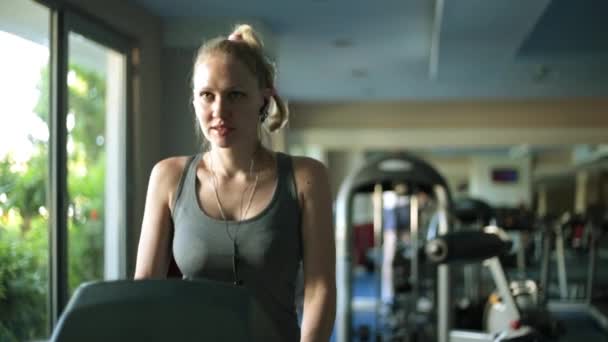 Una mujer atractiva en una cinta de correr. Una chica está entrenando en un gimnasio . — Vídeos de Stock