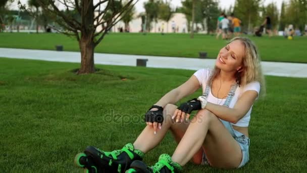 Bella donna in pattini a rotelle sta ascoltando musica nel parco. La bionda sta ascoltando musica nel parco . — Video Stock