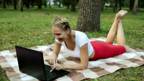 Mujer positiva en el parque con portátil. Chica con portátil en el césped . — Vídeo de stock