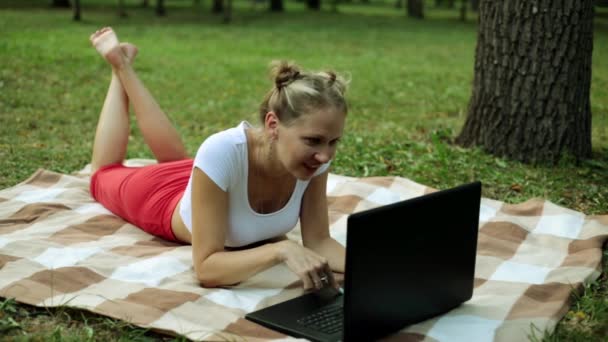Dívka s notebookem na trávníku. Pozitivní žena v parku s notebookem. — Stock video