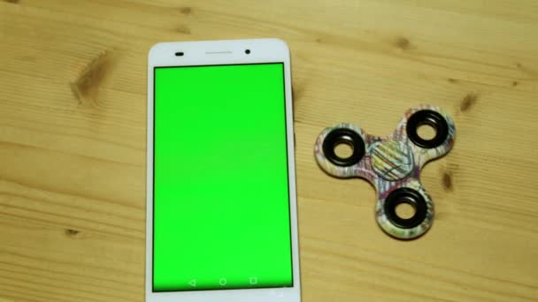 En smartphone med en grön skärm på ett träbord. Leksak spinner och telefon. — Stockvideo
