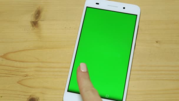 En surfplatta med en grön skärm på ett träbord. En kvinna använder en smartphone med en grön skärm. — Stockvideo