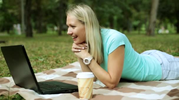 Jonge vrouw met laptop op het gras. Het meisje gaat op skype met behulp van een laptop in het park. — Stockvideo
