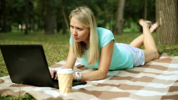 Mujer joven con portátil en el parque. Chica con un ordenador portátil en la naturaleza . — Vídeos de Stock