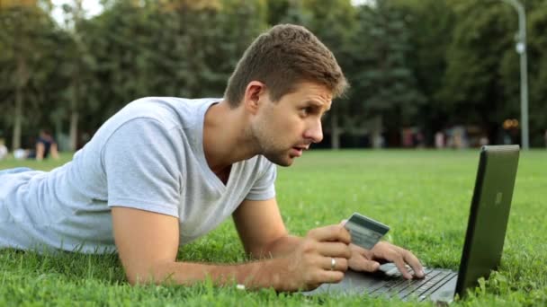 Uma pessoa faz uma compra online por cartão de crédito. Um homem com um portátil e um cartão bancário no parque . — Vídeo de Stock