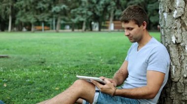 Bir adam parkta bir tablet bilgisayar kullanıyor.