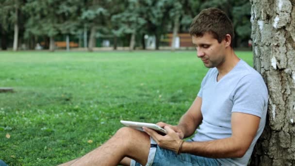 Un hombre está usando una tableta en el parque . — Vídeos de Stock