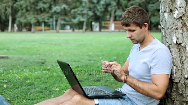 En man med en laptop i parken använder bank kreditkort. — Stockvideo