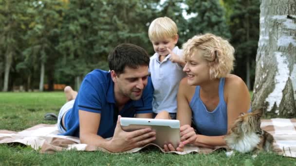 Lycklig familj och digital teknik. Familj med ett barn och en surfplatta i parken. — Stockvideo