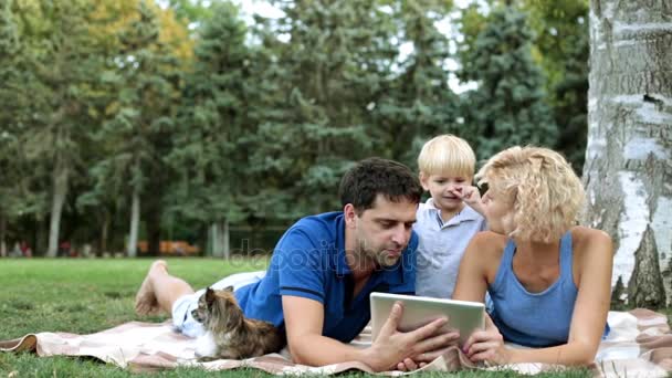 Семья с ребенком и планшетным компьютером в парке. Счастливая семья и цифровые технологии . — стоковое видео