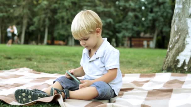 Bir çocuk ile bir smartphone çimenlerin üzerinde bir parkta. — Stok video