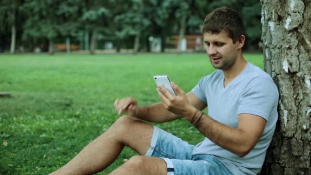 En man med en smartphone i parken. En man på Internet med hjälp av en smartphone i naturen. — Stockvideo