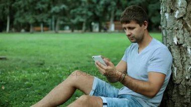 Bir adam parkta bir akıllı telefon kullanır.