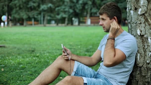 Un hombre en el parque escucha música usando un smartphone . — Vídeos de Stock