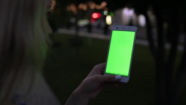 Une femme dans la soirée tient un smartphone avec un écran vert .