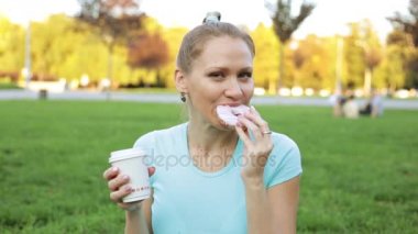 Kız parkta yiyor. çörek yeme ve içme kahve güzel kadın.