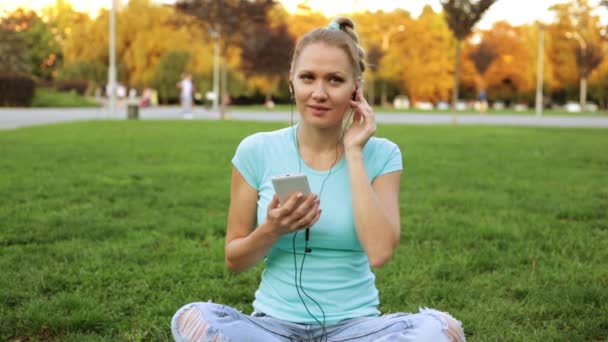 Ung kvinna Lyssna på musik med smartphone i parken. — Stockvideo