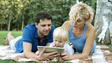 Çocuk bir tablet bilgisayar ile oynuyor ve veliler yan yana oturuyor.