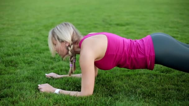 En kvinnlig idrottare skakar musklerna i pressen, en övning ombord. En ung kvinna som är engagerad i fitness i parken. — Stockvideo
